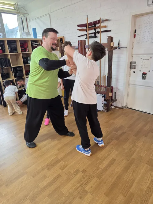 Prüfungssituation im Dao Wing Chun: Trainer korrigiert Technik eines Kindes