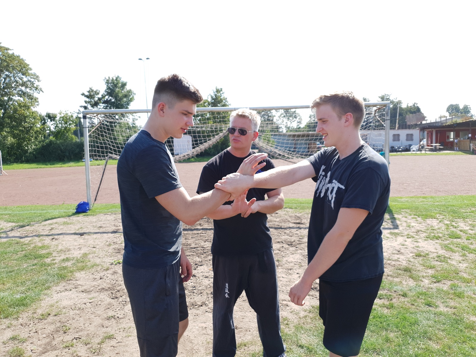 Trainer korrigiert zwei Schüler bei einer Wing-Chun-Grifftechnik im Freien