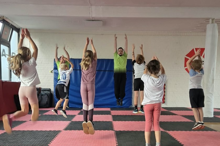 Selbstverteidigung für Kinder 12 Kinder und Trainer beim gemeinsamen Sprung-Warmup im Training